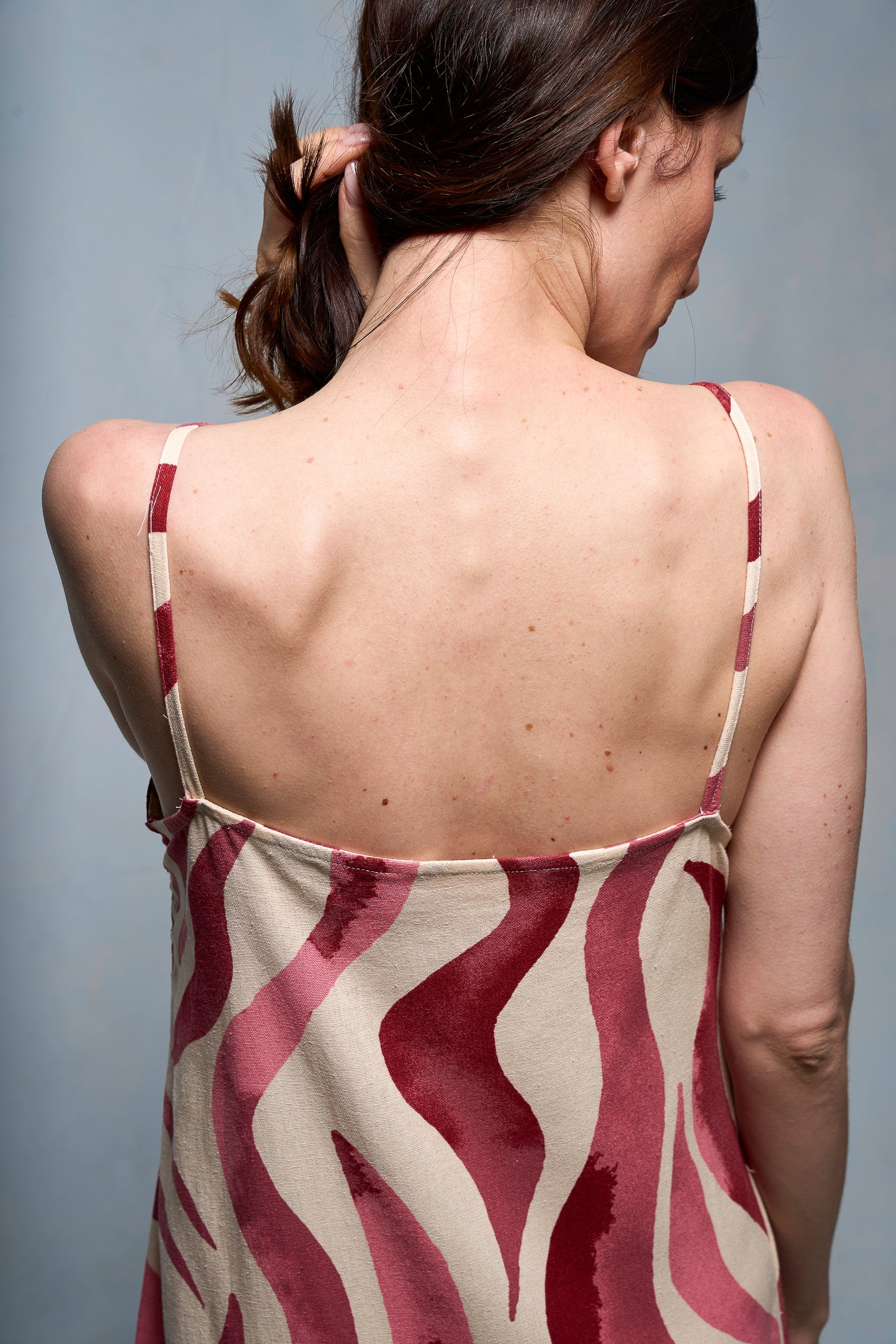 Espalda de mujer sujetándo su cabello, vestida con slipdress color fucsia.